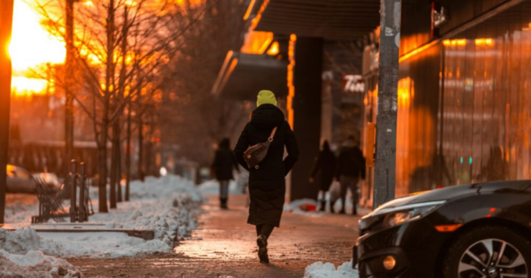 Person walking on snowy sidewalk with a sunset in the background