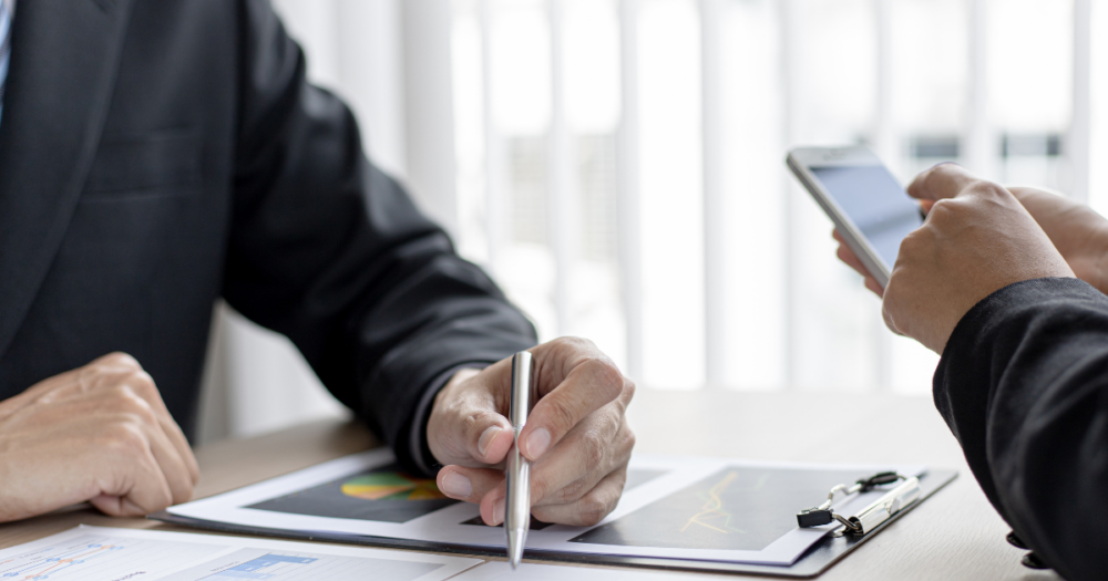 A meeting with two people, one overlooking a chart, another on their phone